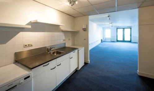 Keuken en open ruimte in een kantoor- of woonruimte aan de Hoogte Kadijk, met wit interieur en blauwe vloerbedekking.